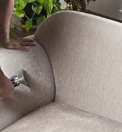 Professional upholstery cleaner deep-cleaning a fabric sofa with a handheld extraction tool and hose Albany, NY.